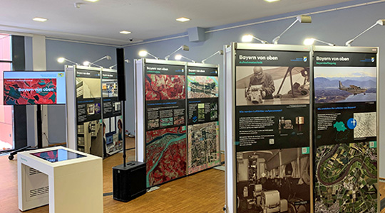 Bild aus der Ausstellung. Auf dem Bild sind verschiedene Infotafeln mit Luftbildern zu sehen.